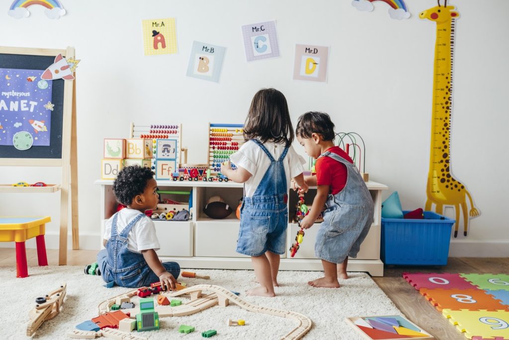 Young children play together with toddler toys in a colorful playroom.